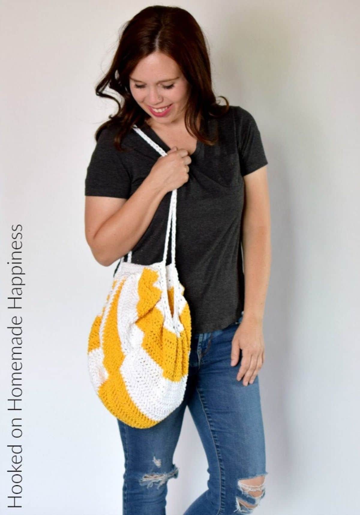 Dark haired woman standing with a white and mustard yellow crochet round bag with long thin straps. 