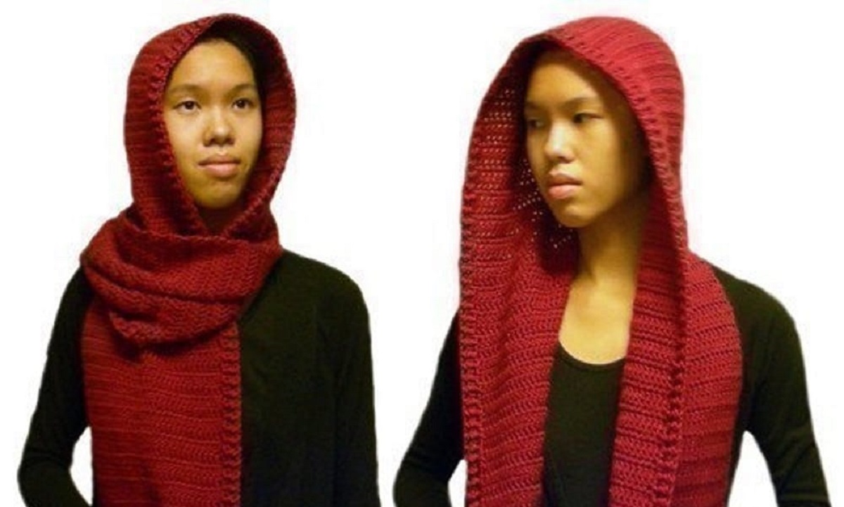 Woman wearing a red crochet hooded scarf wrapped around her neck and a black jumper.