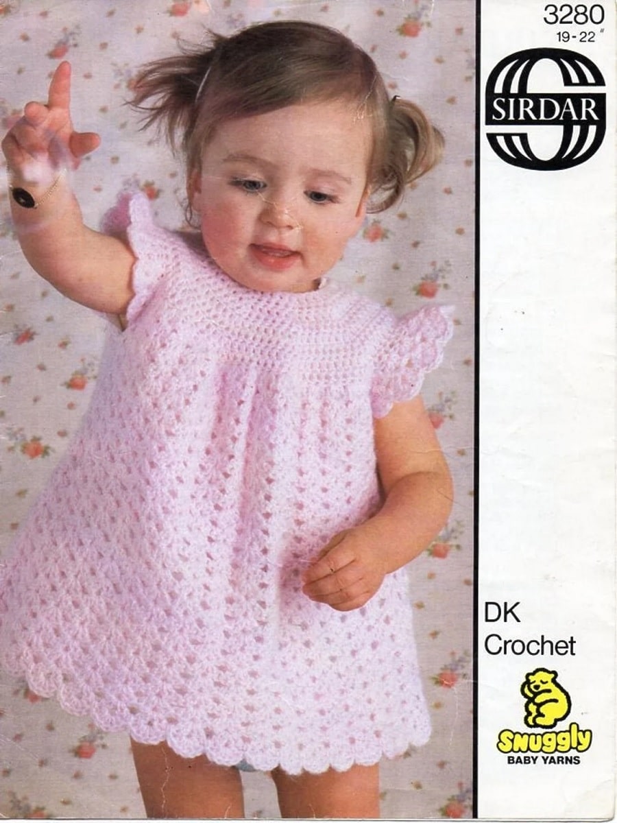 Brunette toddler wearing a short sleeved pink crochet dress with a scalloped edging along the bottom.