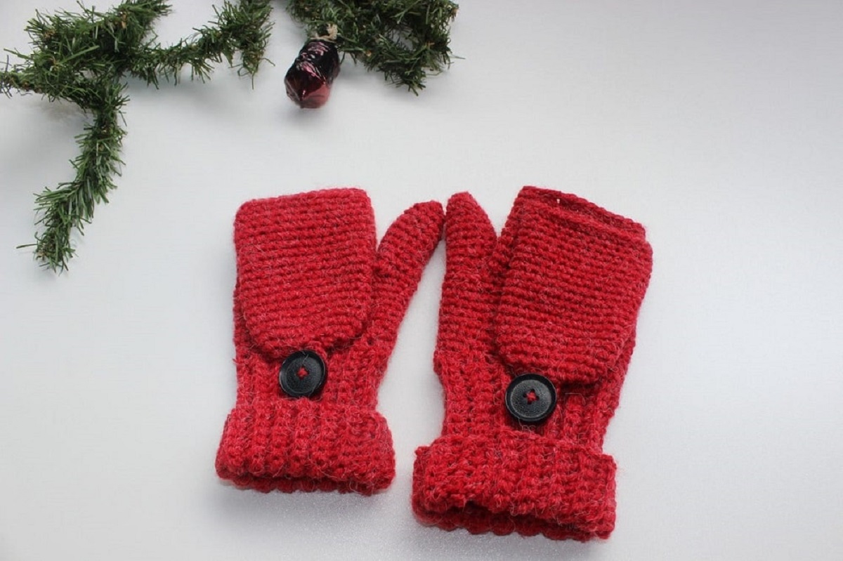 A pair of red crochet gloves with flaps buttoned down that convert into mittens on a white background.