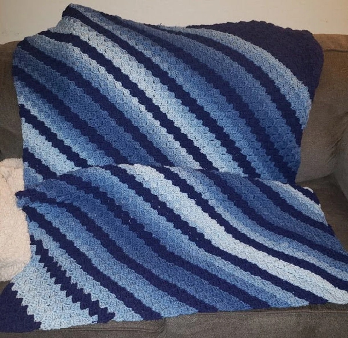  Large corner to corner throw with dark blue, light blue, and white diagonal stripes draped over a brown sofa. 