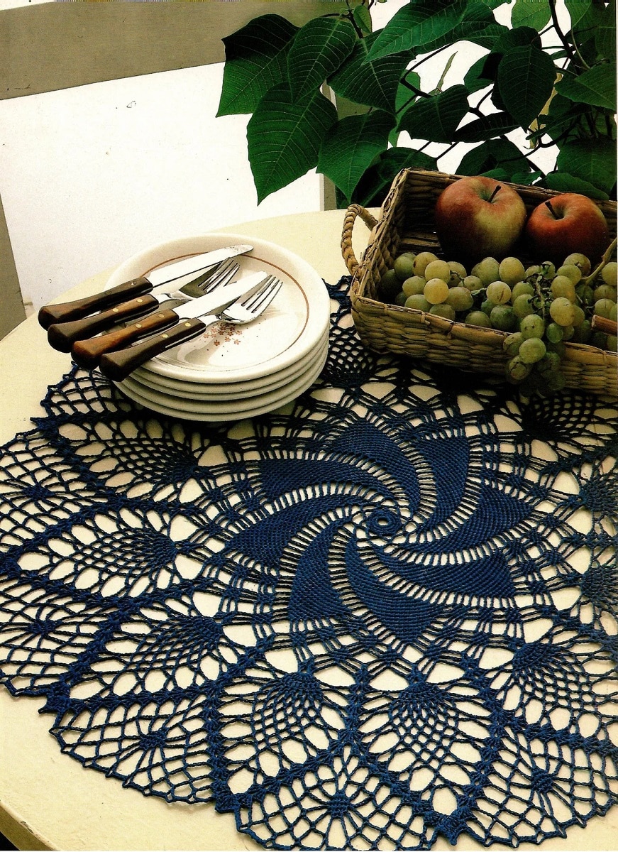 Black crochet doily with a star in the center and loosely weaved pineapples in petals around the outside on a wooden table.