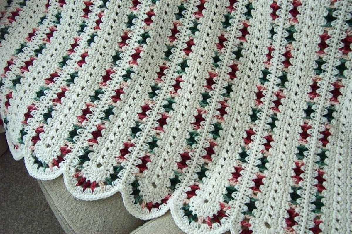 White crochet rounded afghan with red and green stitching running vertically placed on a cream sofa.