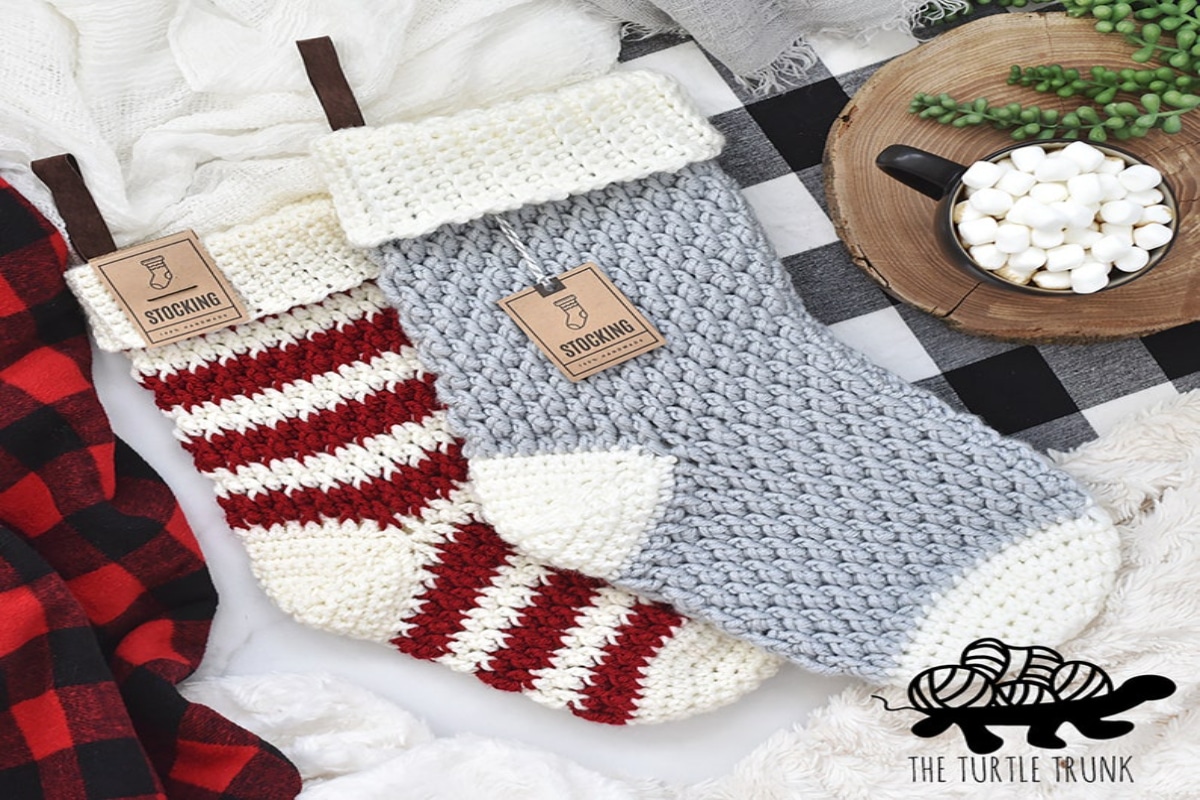 Pale blue and white crochet stocking sitting on red and white striped stocking and black and white checkered stocking on a white background. 