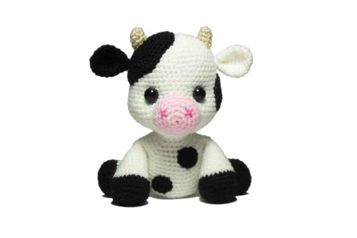 Small black and white crochet calf with black spots on its belly, black feet, and one black ear sitting with its back legs spread behind him.