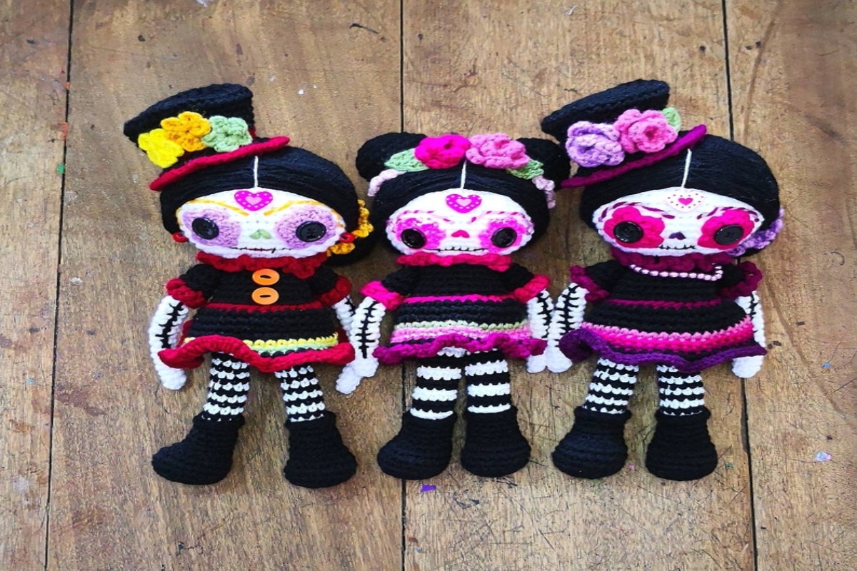 Three crochet skeleton dolls wearing black dresses with black and white striped legs, pink flowers for eyes, and flowers in their hair.