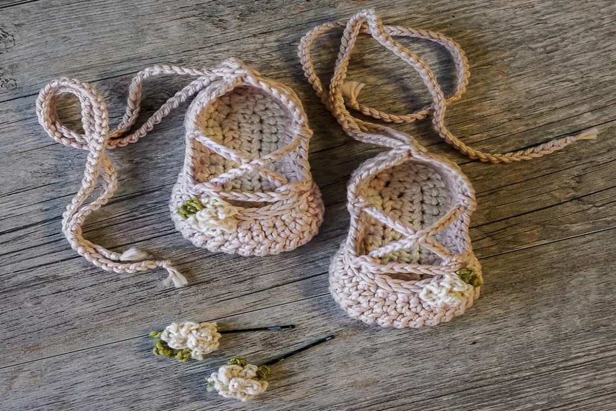 Pale pink and yellow crochet baby ballet slippers with yellow and white crochet flowers on the top, a crossover design on the foot and long straps to secure.