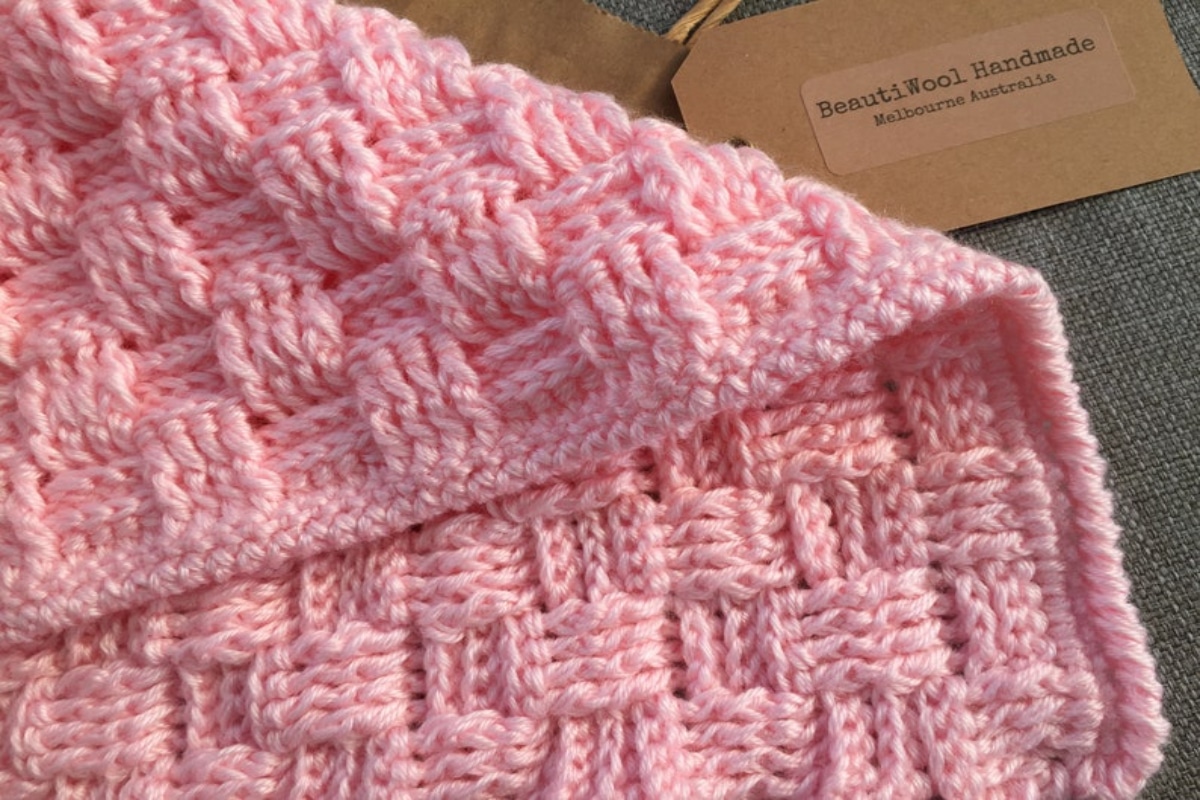 Baby pink crochet baby blanket with a basketweave pattern and small pink vertical trim on all sides.