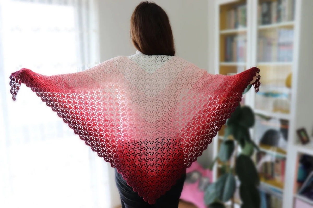 The back of a woman with a pink and cream ombre style crochet shawl with diagonal stripes standing in a home office.
