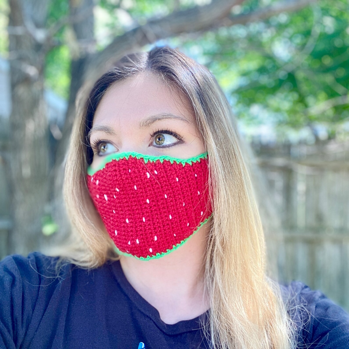 Blond woman wearing a strawberry design facemask with a green trim and red center with small white dots all over it.