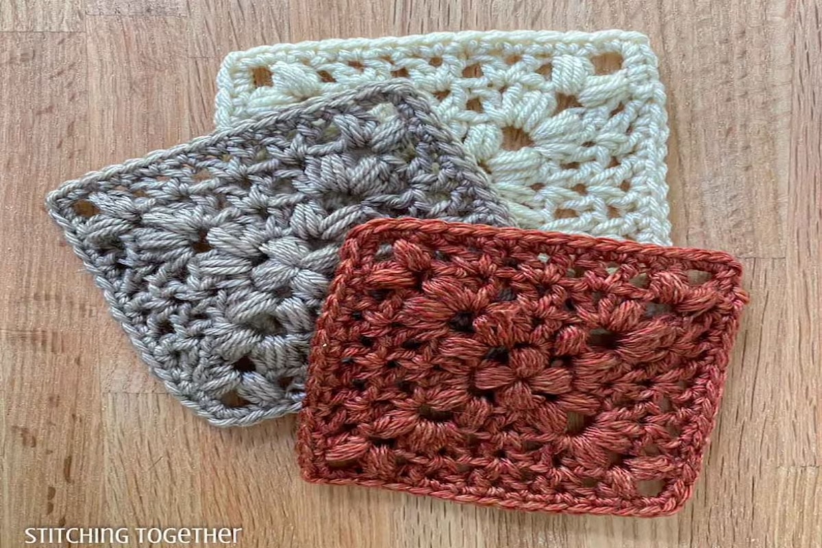 Rust colored crochet granny square on top of a gray and cream square with the same pattern on a wooden background.
