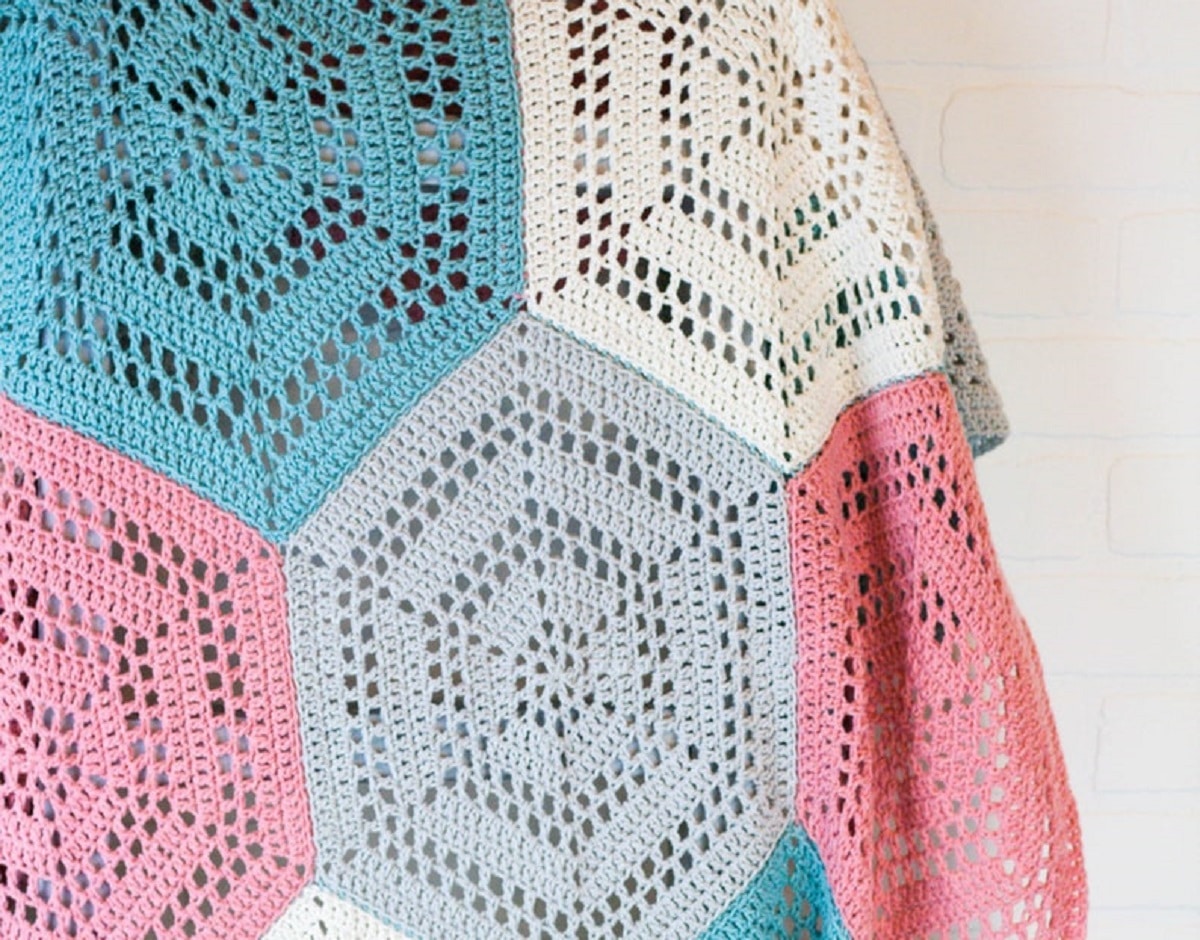  A large crochet blanket using cream, blue, light gray, and pink hexagon patches with smaller hexagons in each patch.