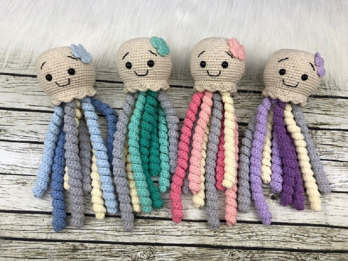 Four small crochet jellyfish with beige heads and thick blue, purple, pink, blue, and green tentacles dangling from their heads.