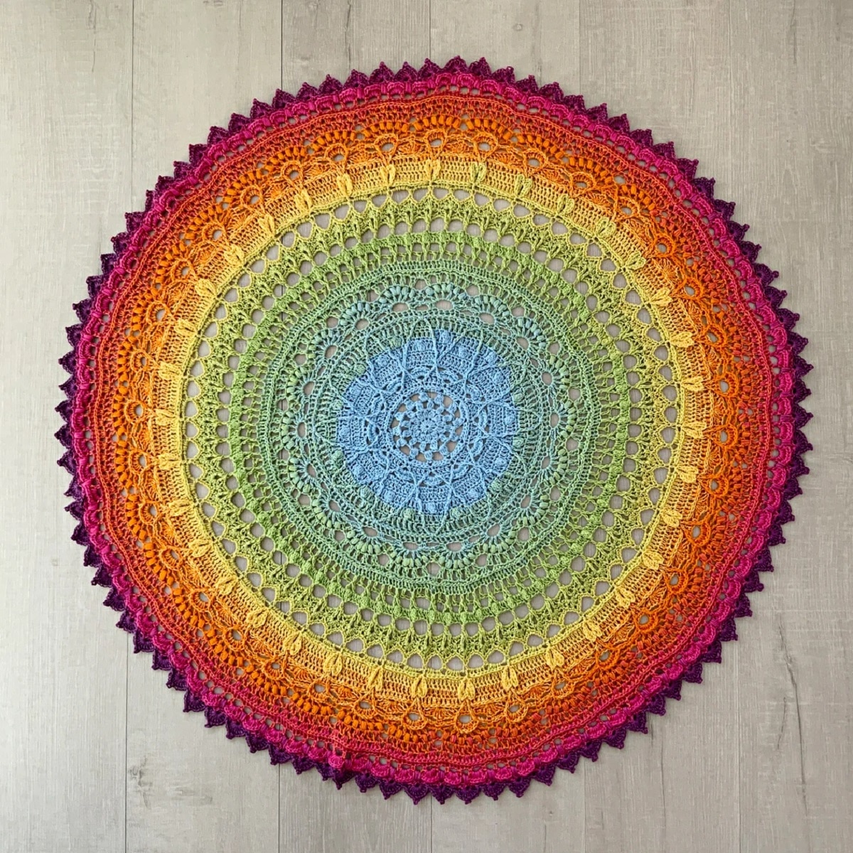 Large crochet circle doily with a purple trim, and red, yellow, orange, and green circles with a blue flower in the center.