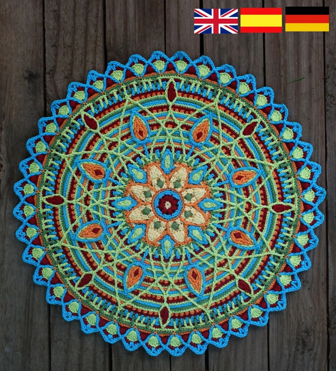  A blue, green, red, and orange round crochet doily with a large mandala in the center on a gray wooden floor.