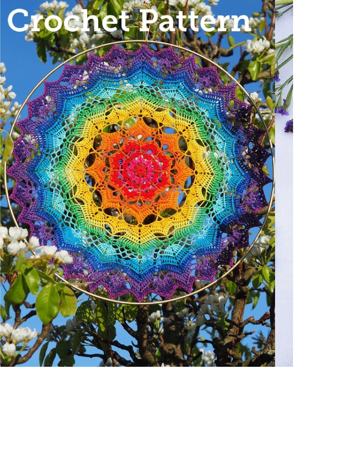 A rainbow colored crochet mandala doily next to some green leaves and small white flowers. 