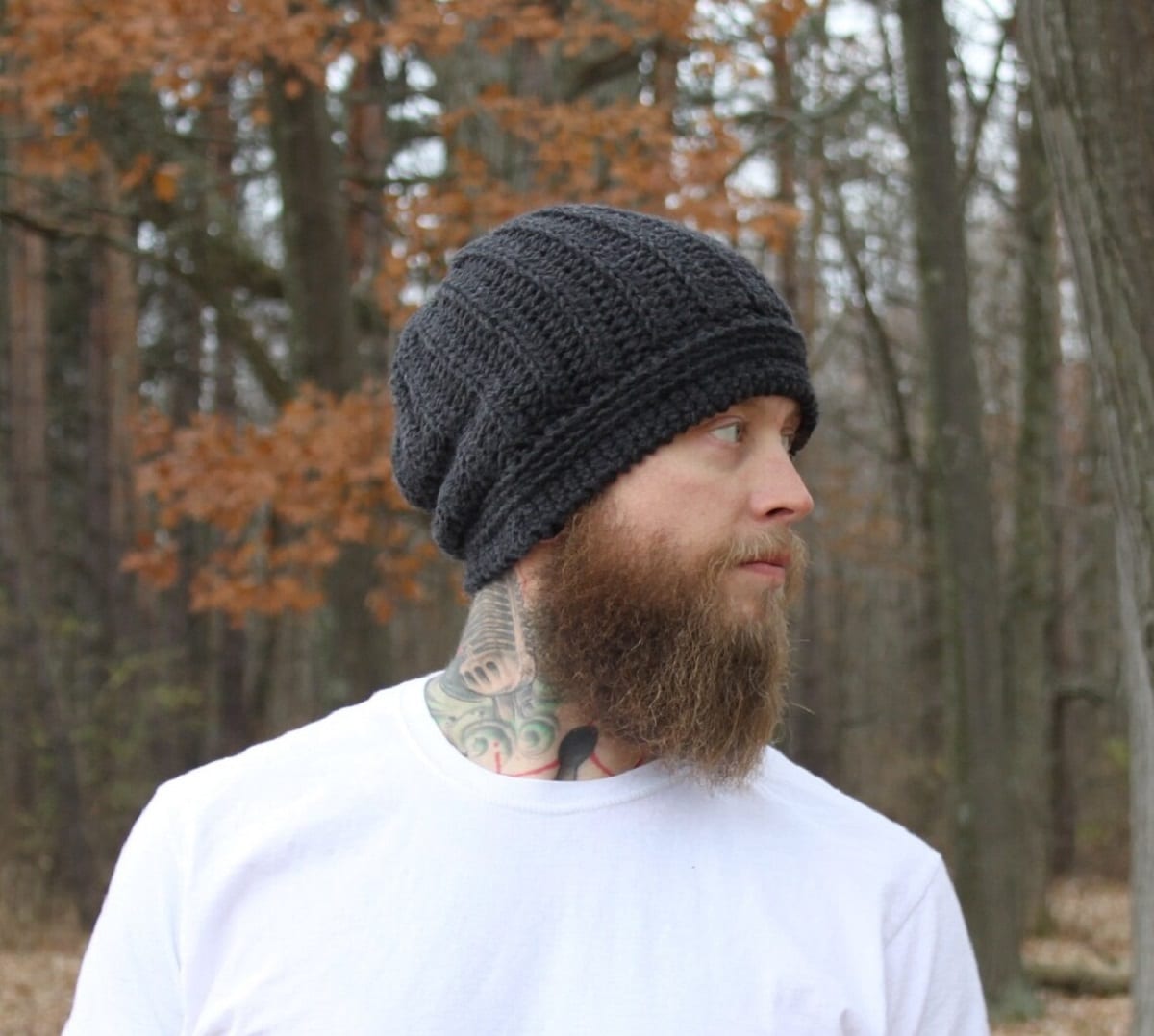 Bearded man in a forest wearing a black slouchy crochet beanie and a white top.
