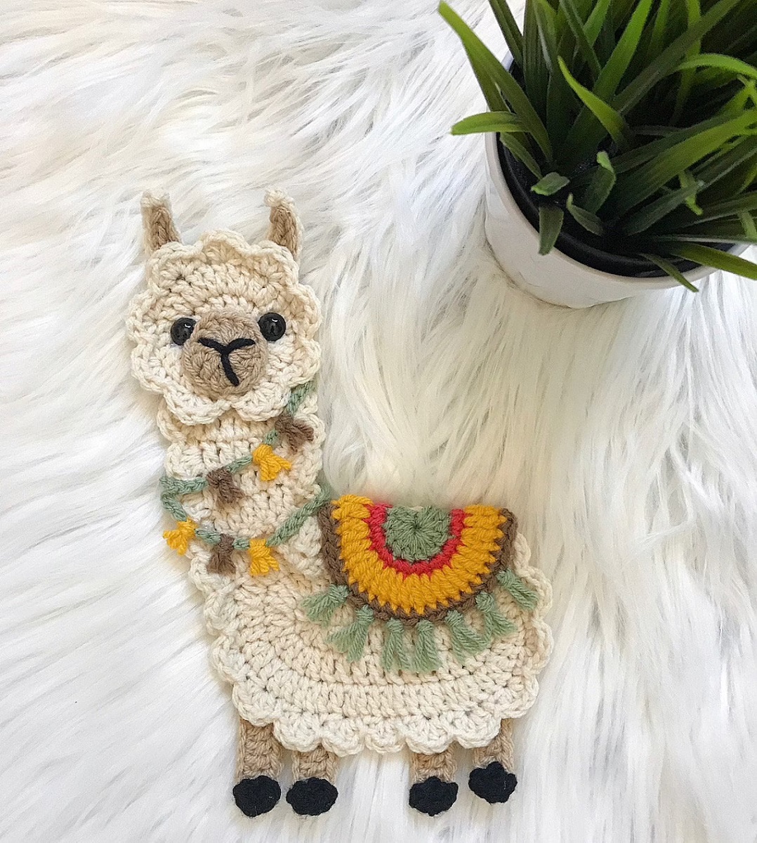 Flat crochet cream llama with a doily style face and body and teal and yellow tassels around its neck and the seat on its middle.