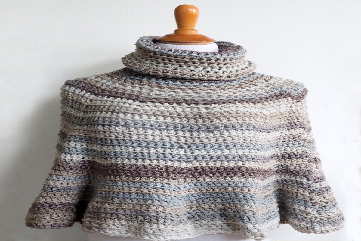 A multi-colored striped poncho. Rows of grey, blue, and purple run across the poncho which features a high roll neck.
