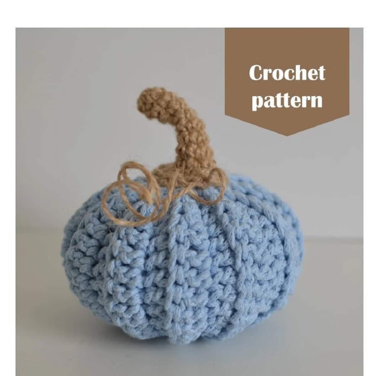 Small blue crochet pumpkin with a brown stem at the top on a white background.