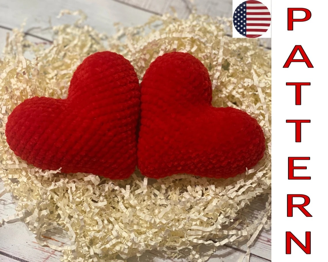 Two textured small red crochet hearts stuffed and placed next to each other on a bed of pale yellow tissue paper.
