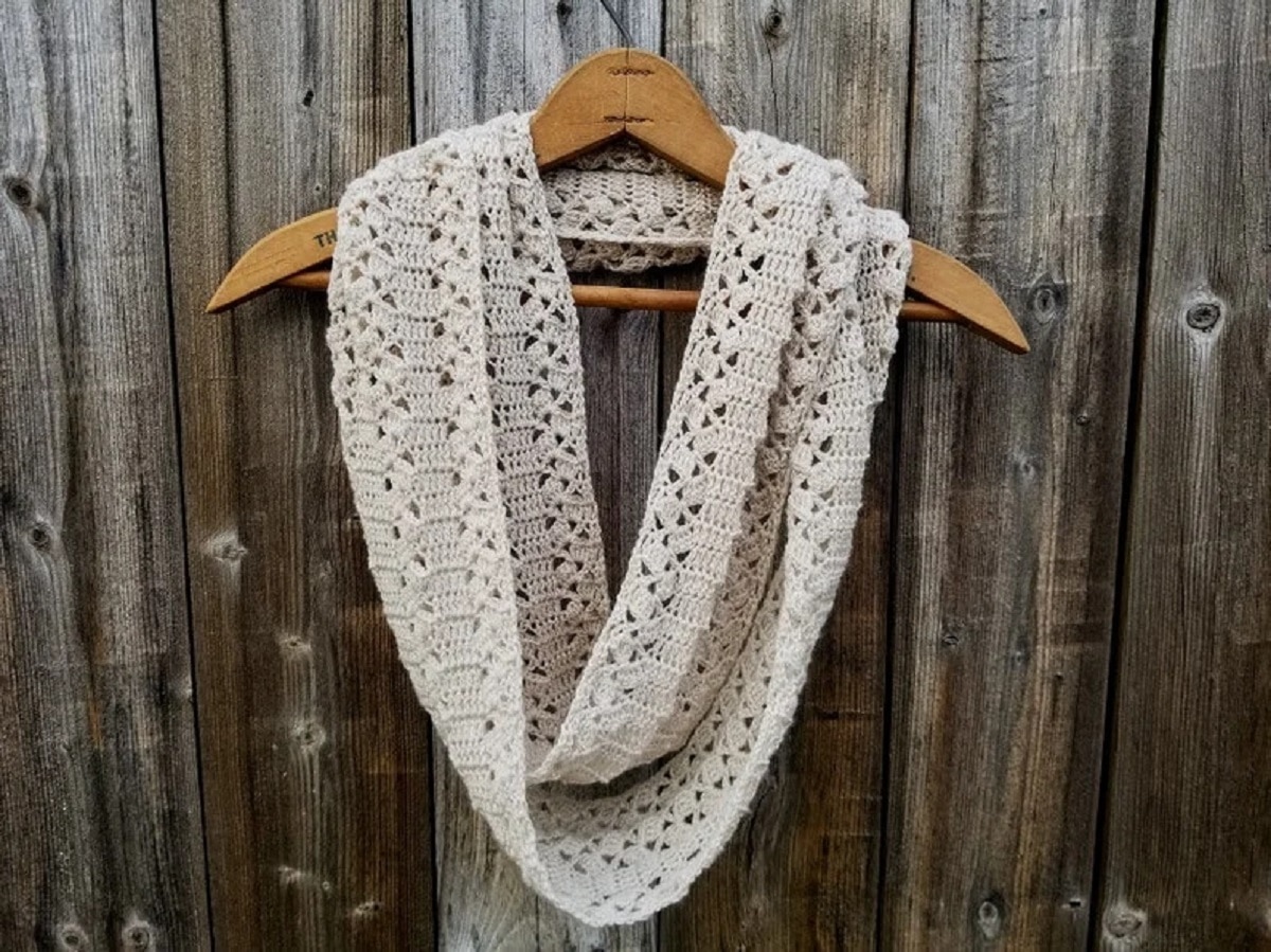 Beige crochet lace style scarf folded over a wooden hanger against a gray wooden background.