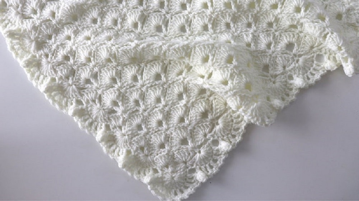 The corner of a cream crochet blanket with a shell pattern and small trim on a white background.