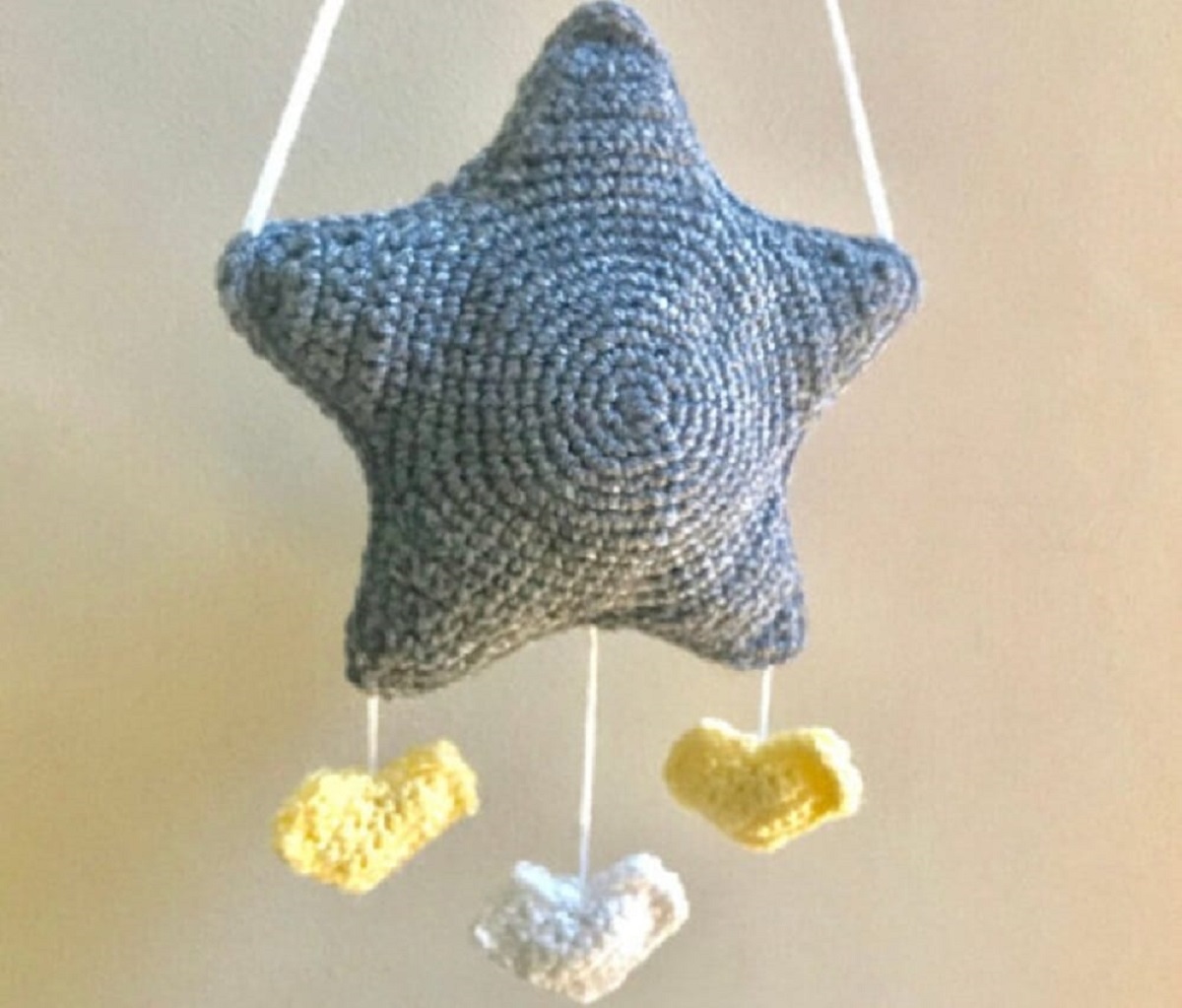 A stuffed crochet blue star mobile with three yellow birds hanging from the bottom of the star on a beige background.