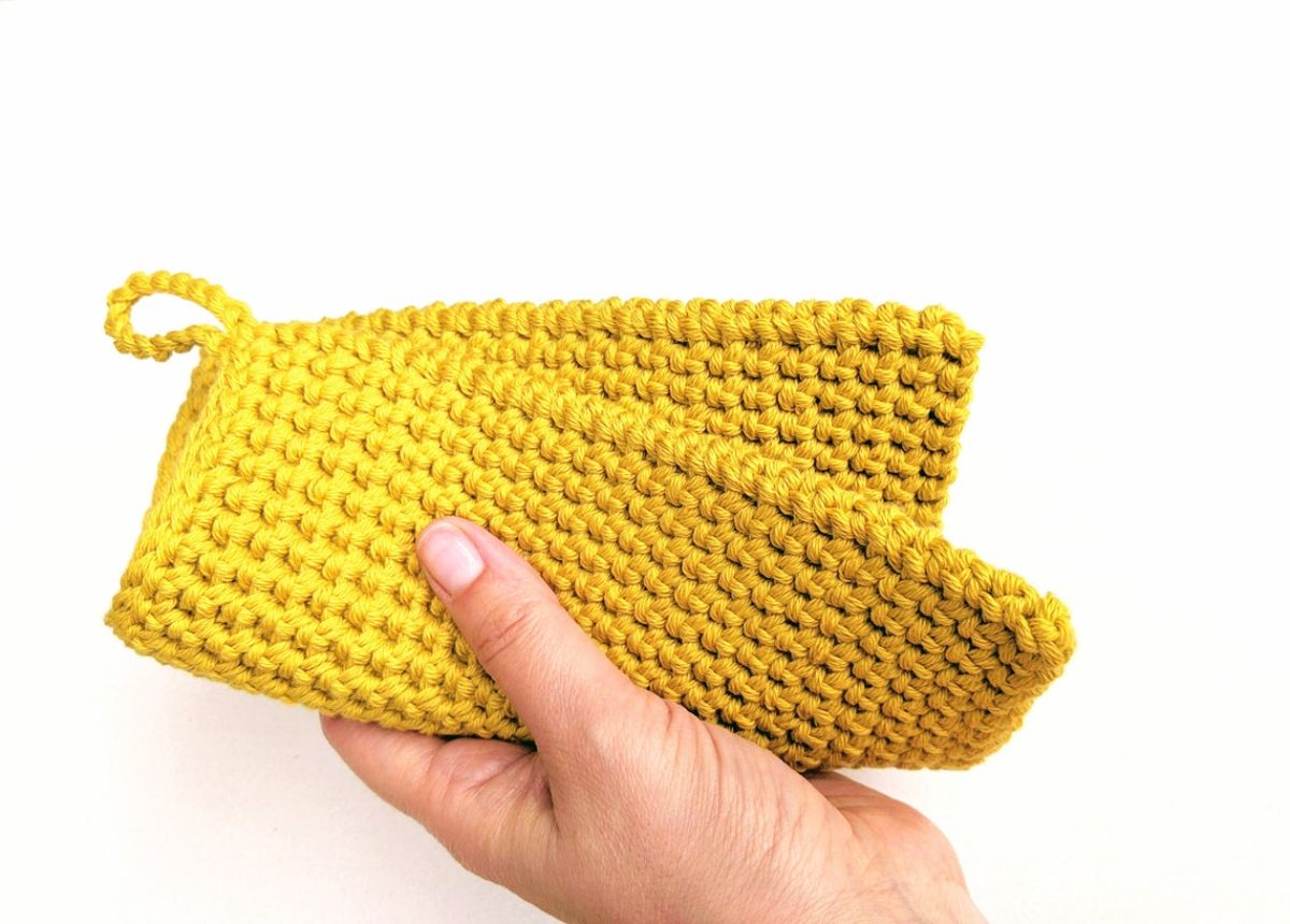  A hand holding a folded over yellow crochet hot pad with a small yellow loop at the top.
