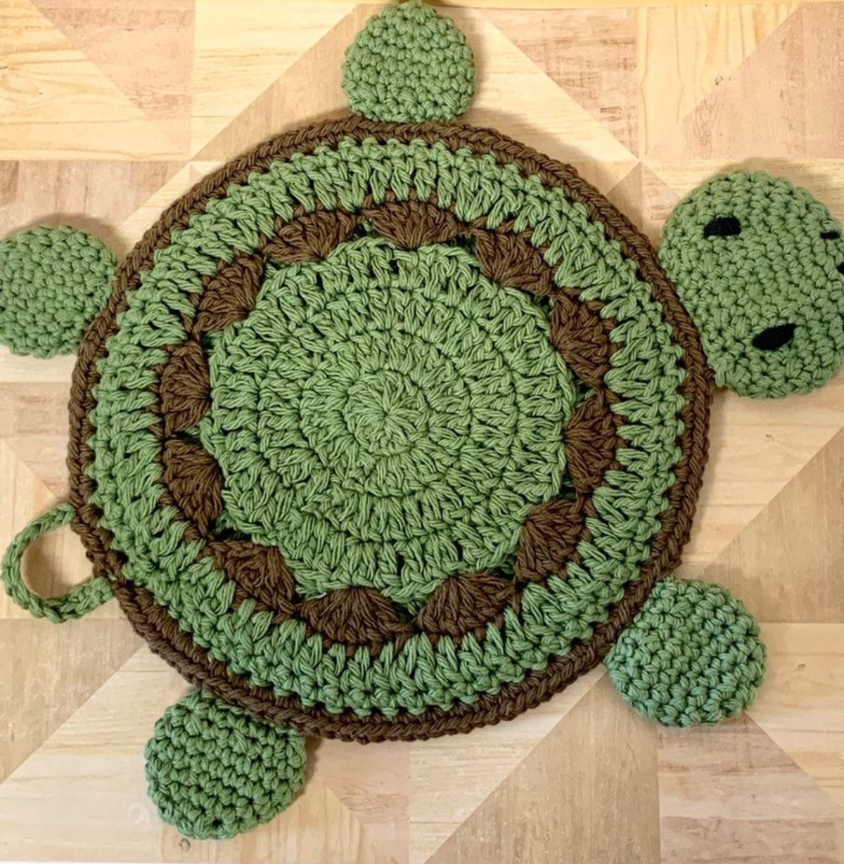 Large green and brown turtle shaped crochet pot holder on a wooden countertop.
