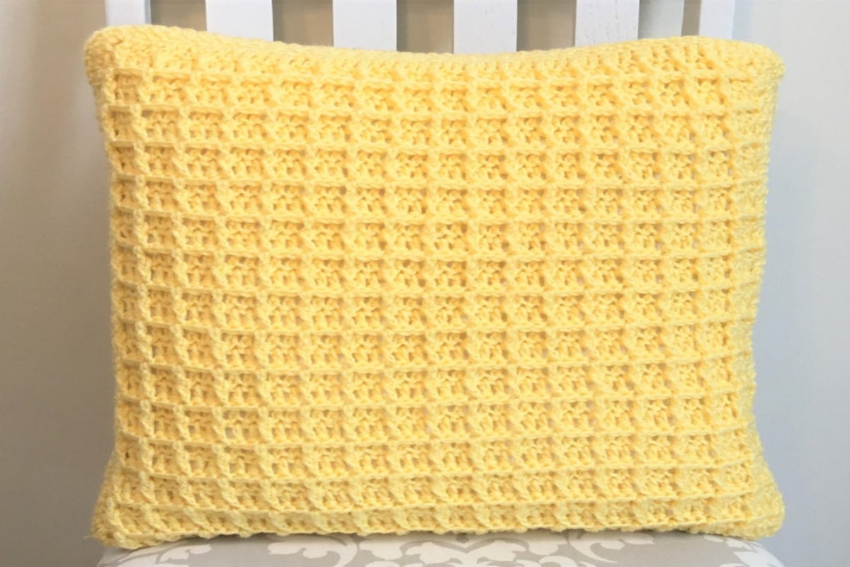 Yellow crochet stuffed rectangular waffle stitch cushion placed on a white chair with a white background. 