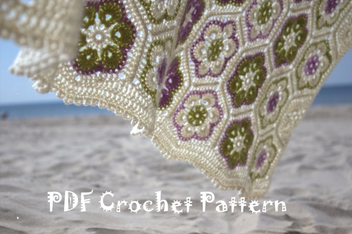 The bottom of a cream crochet blanket with pink and green African flowers stitched into the blanket in horizontal rows.