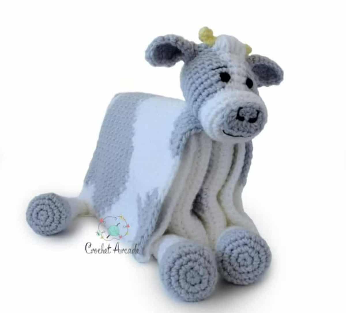 Blue, gray, and white crochet blanket with a stuffed cow's head and legs, folded to look like the cow is sitting down.