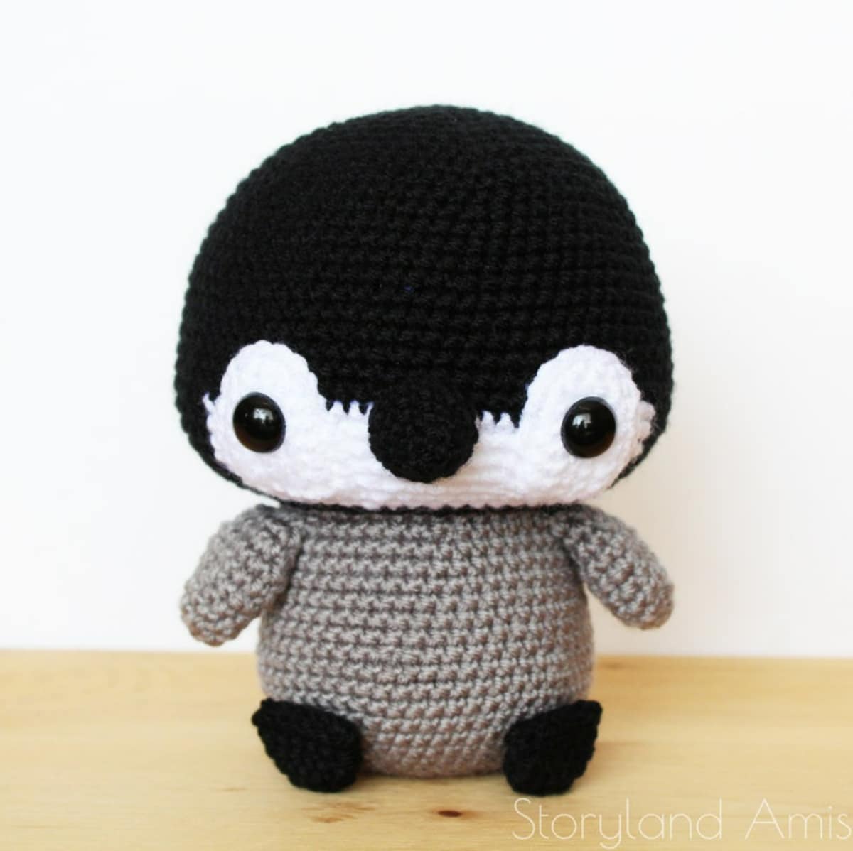 Large crochet penguin with an oversized black and white face with a black bobble for a nose and a gray body.