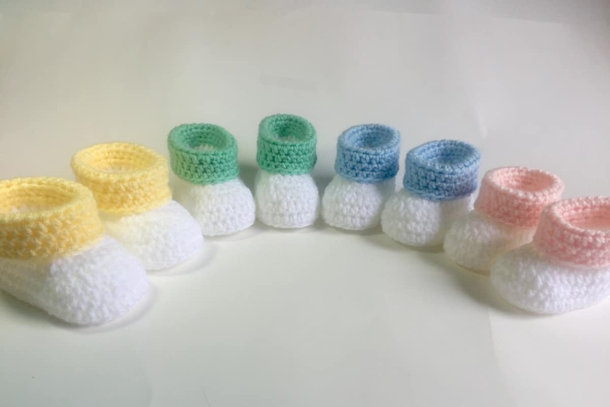 A semi circle of white baby booties with different color tops. There are yellow, green, blue, and pink booties.