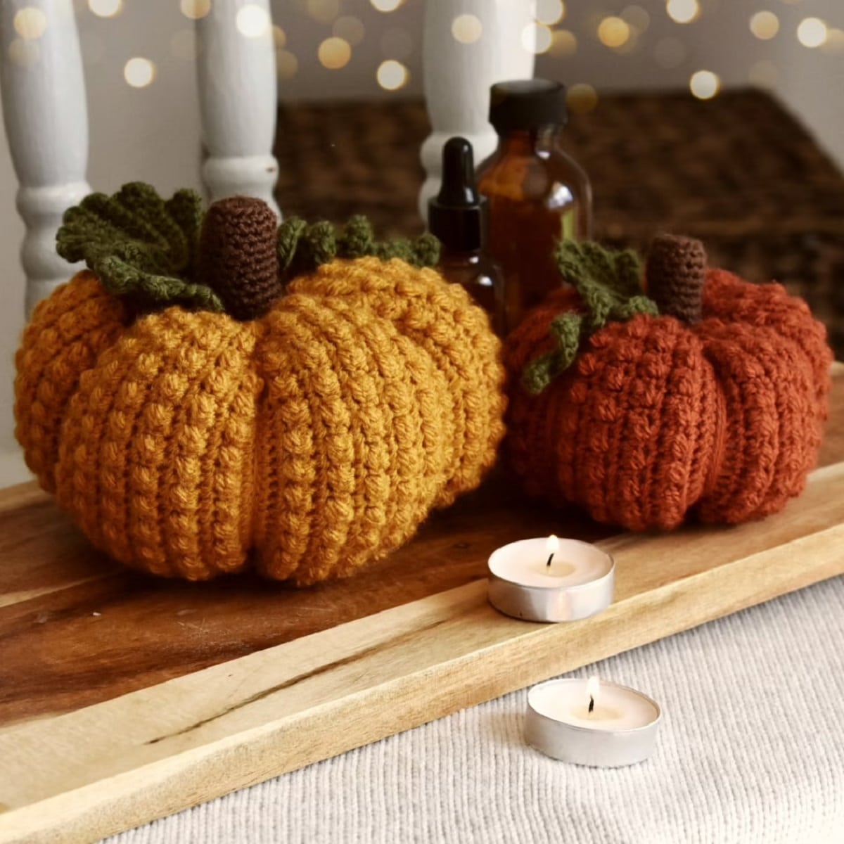 A light orange crochet pumpkin with bobbles all over next to a dark orange pumpkin with the same pattern.