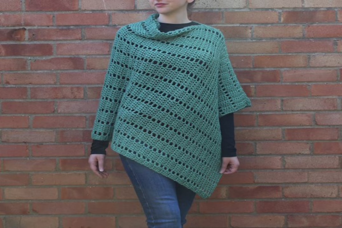 Woman wearing a teal colored crochet poncho with a diagonal hem, one long sleeve, and one half sleeve.