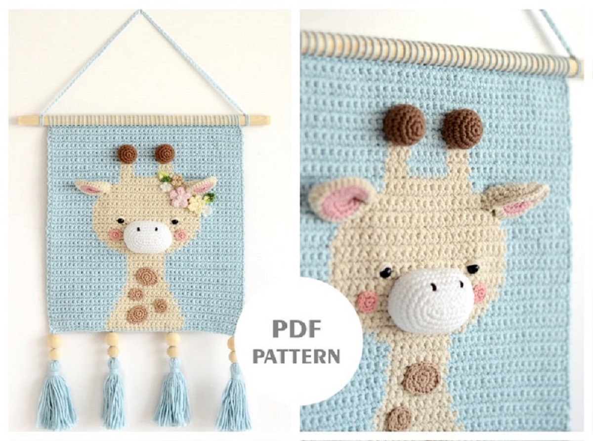 A light blue crochet wall hanging with a large yellow and brown spotted giraffe in the center with a 3-D white nose.