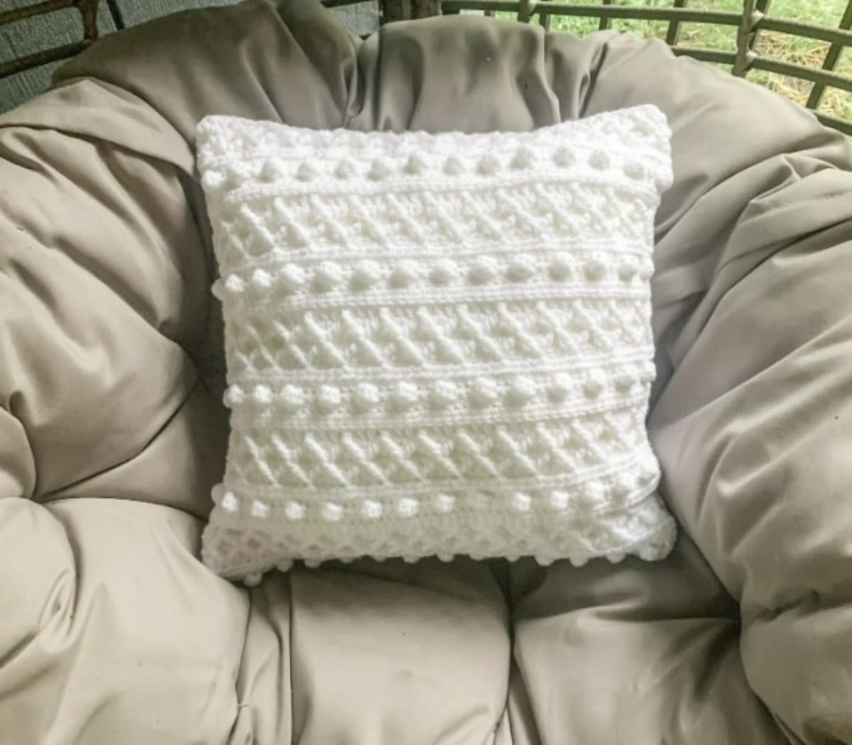 White crochet cushion with alternating rows of diamond shape pattern and small white bobbles on a gray chair.