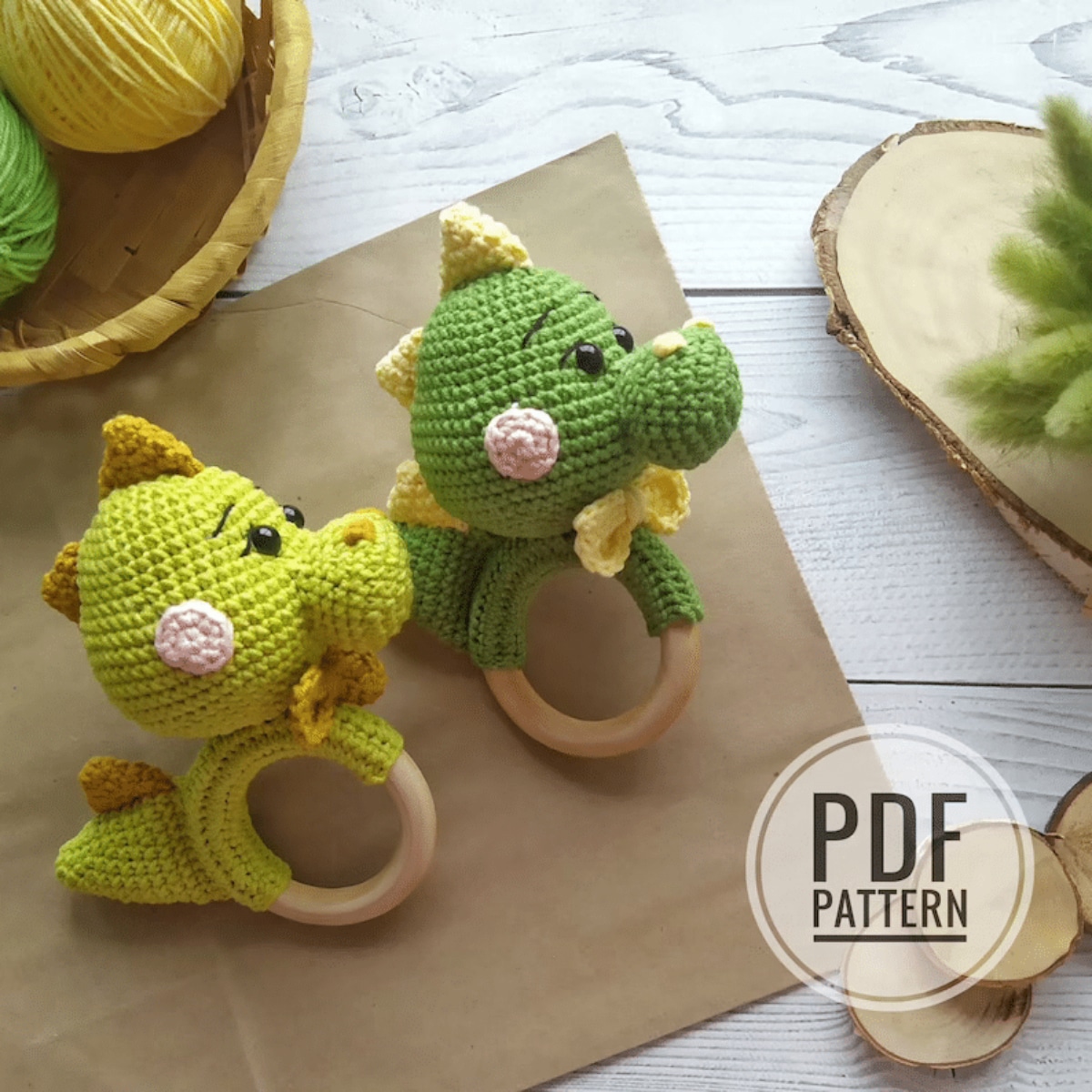 A lime green crochet dinosaur rattle with brown spikes on its head and tail next to a dark green dinosaur rattle with the same pattern.