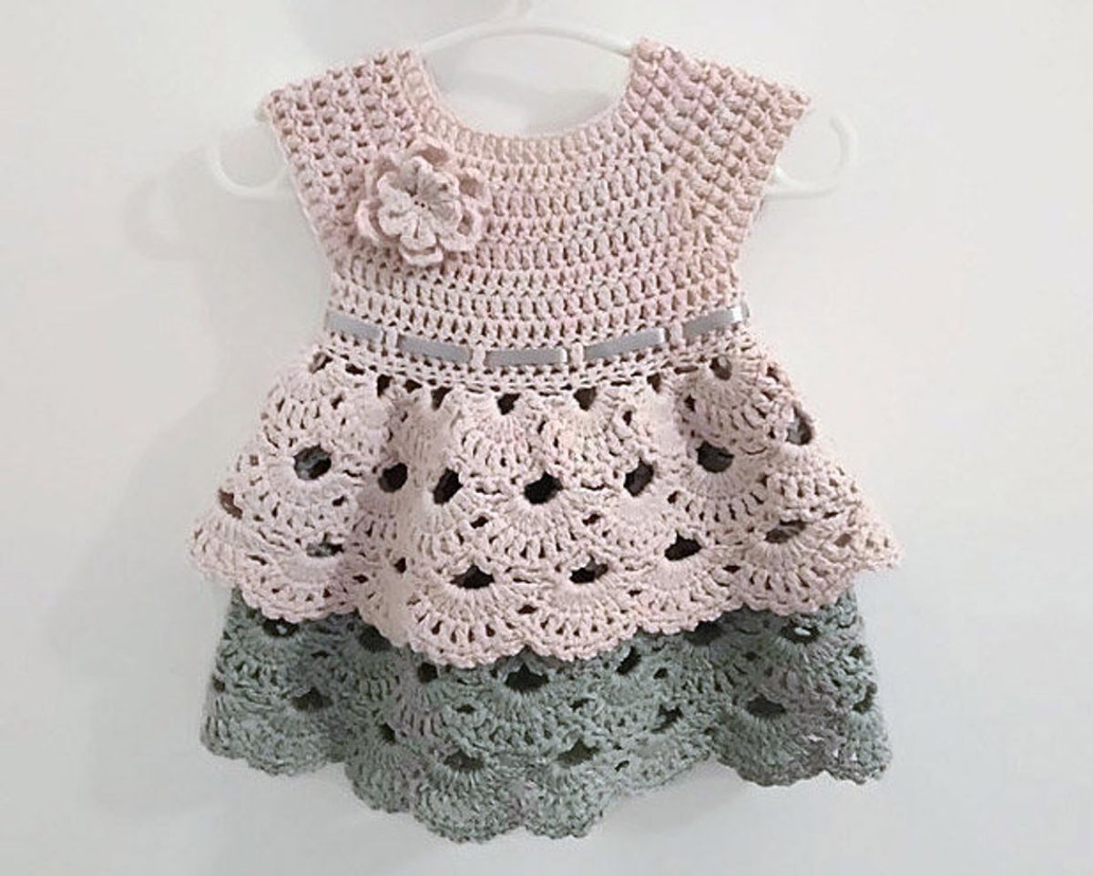 Beige and green crochet baby dress with short sleeves, a beige flower, and a ruffle skirt with beige and green ruffles.