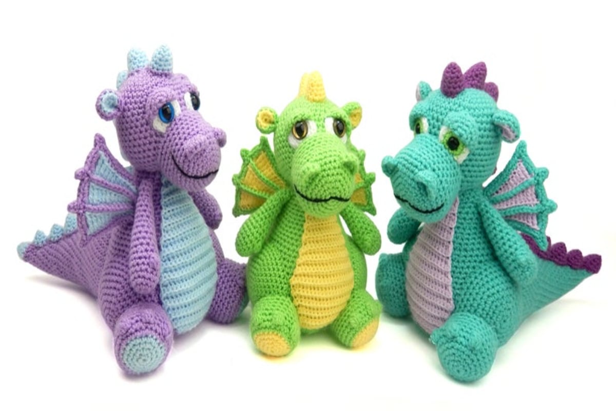 A purple and blue crochet stuffed dragon sitting next to a green and yellow and an aqua and purple dragon.