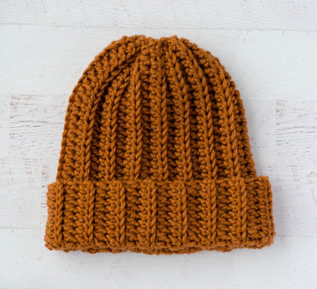  A rust colored beanie with a chunky crochet pattern and thick trim on a white background.