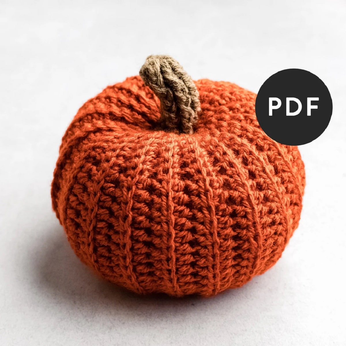 A small brown ribbed crochet pumpkin with a brown stem in the middle on a white background.