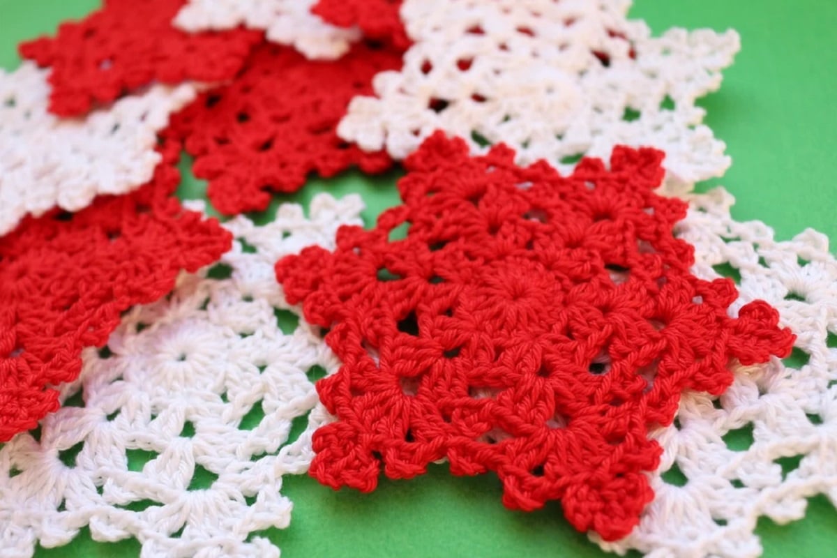 A small pile of red and white crochet snowflakes lying on top of each other on a green background.