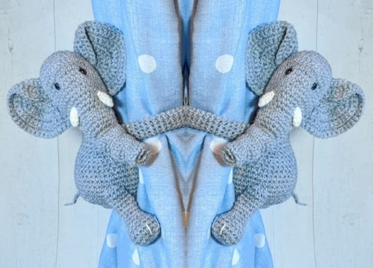 Grey and blue crochet Elephant curtain tie backs wrapped around a blue curtain with small white spots.