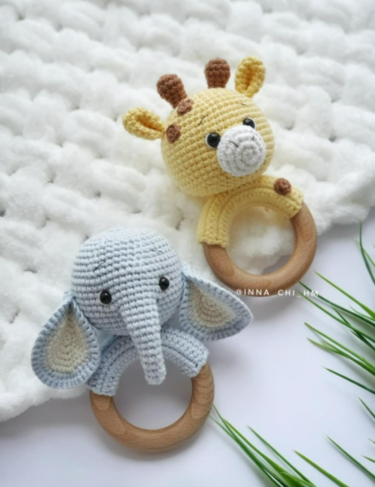  A small gray crochet elephant baby rattle next to a yellow and brown giraffe rattle lying on a white crochet blanket.