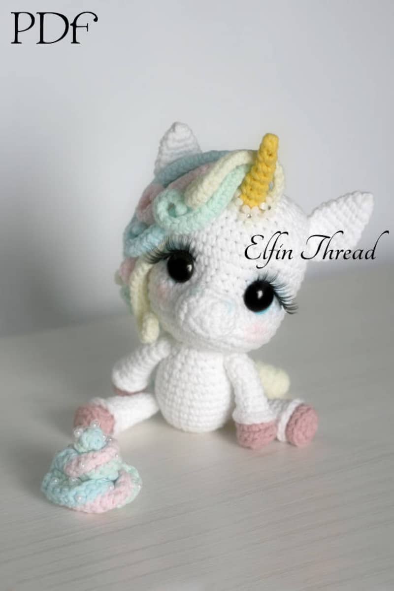 Small white crochet unicorn with a yellow horn, pastel colored hair and pale pink feet, with stuck on eyelashes.