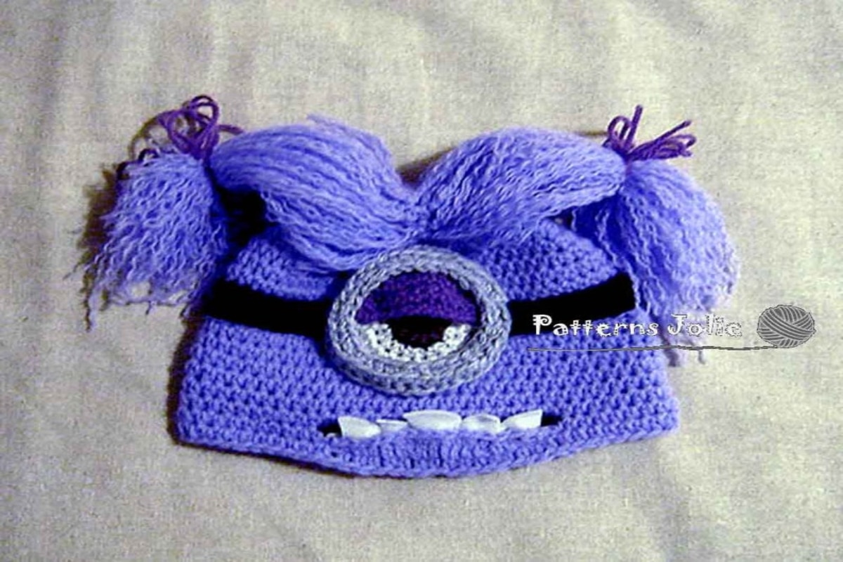 Purple crochet evil minion hat with one gray eye, purple bunches and white wonky teeth for a mouth.