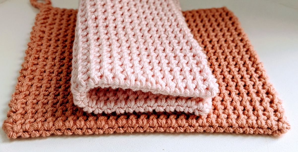 A large orange crochet pot holder with a pale pink pot holder folded in half on top of it.